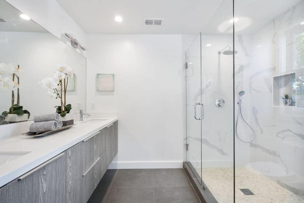 A white bathroom with a walk-in shower enclosure made of clear thick glass panels.