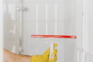 A hand using a squeegee to remove water spots and streaks from a shower door, demonstrating the best way to clean shower screens.