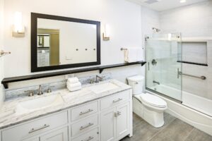 A modern bathroom featuring a white vanity with dual sinks, a large mirror, and a marble countertop. The focal point is the bathtub with a glass shower screen, equipped with a sliding door. The sleek design and clean lines highlight the benefits of shower screens for bathtubs, offering both functionality and a contemporary aesthetic.